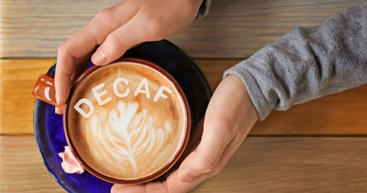 Decaf coffee latte with “decaf” text in foam held over a wooden table
